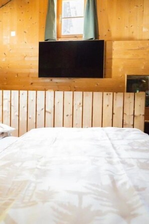 A room with a bed, wooden walls, a mounted television, and a window with curtains. - Turmhaus Giovanoli, (Tschlin) by Interhome (Tschlin)