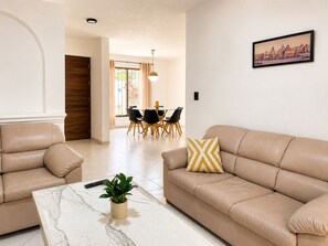 Een woonkamer met een bank, een salontafel en een eethoek met stoelen en een tafel.