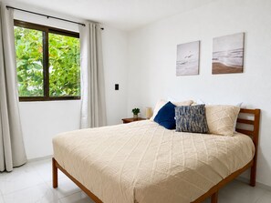A bedroom with a bed, curtains, a window, a nightstand, and wall art. - Gupy 26 - 3BR house steps from de beach  (Cancún)