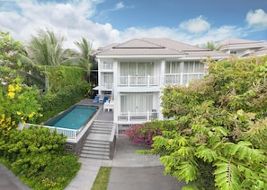 A two-story building with a swimming pool, surrounded by lush greenery and a clear sky. - Koaniva Premier Village Danang (Ngu Hanh Son)