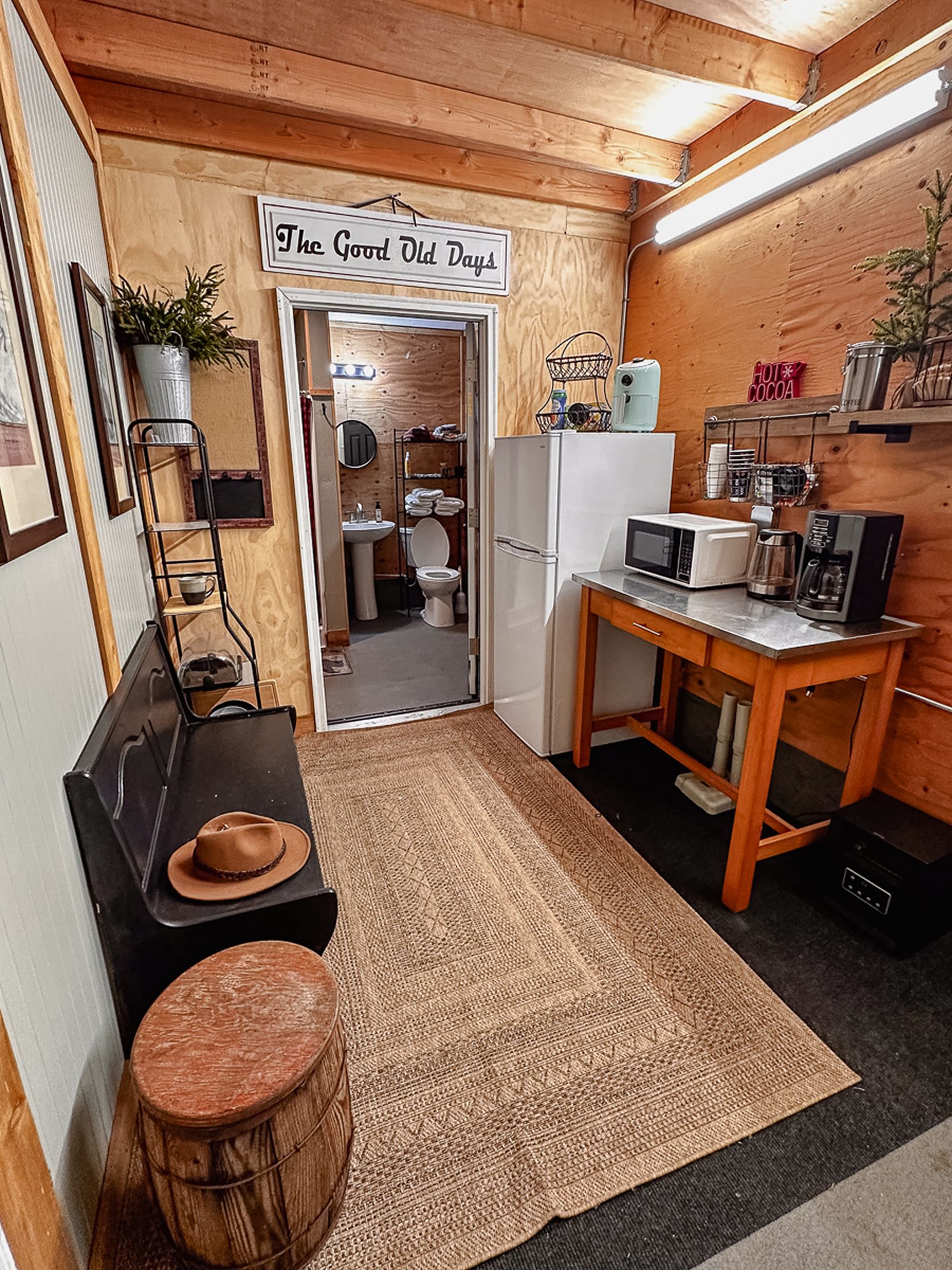 Una cocina compacta con interior de madera, un cartel que dice 'The Good Old Days' y comodidades básicas como refrigerador, microondas y cafetera.