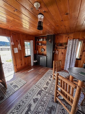 Een houten interieur met vloer, een eettafel, een stoel, een keuken met een koelkast, en een raam met gordijnen.