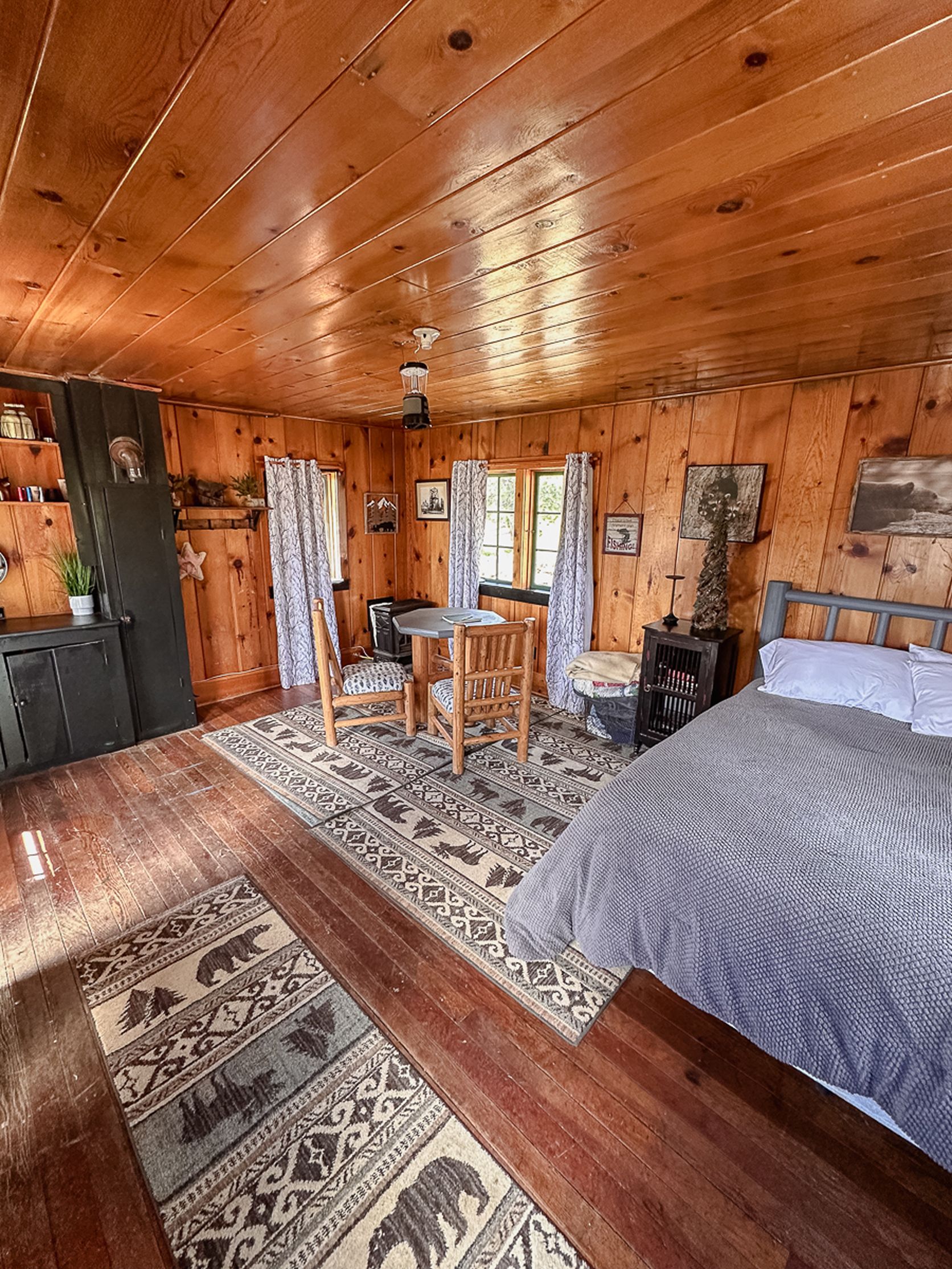 Ein Holzblockhaus-Interieur mit einem Bett, einem Esstisch, Stühlen, einem Kamin und einem Teppich.
