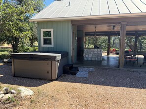 A covered outdoor area with a hot tub, stone fireplace, and a patio table. - Cozy 1-bedroom house in adorable Harper with cool AC (Harper)