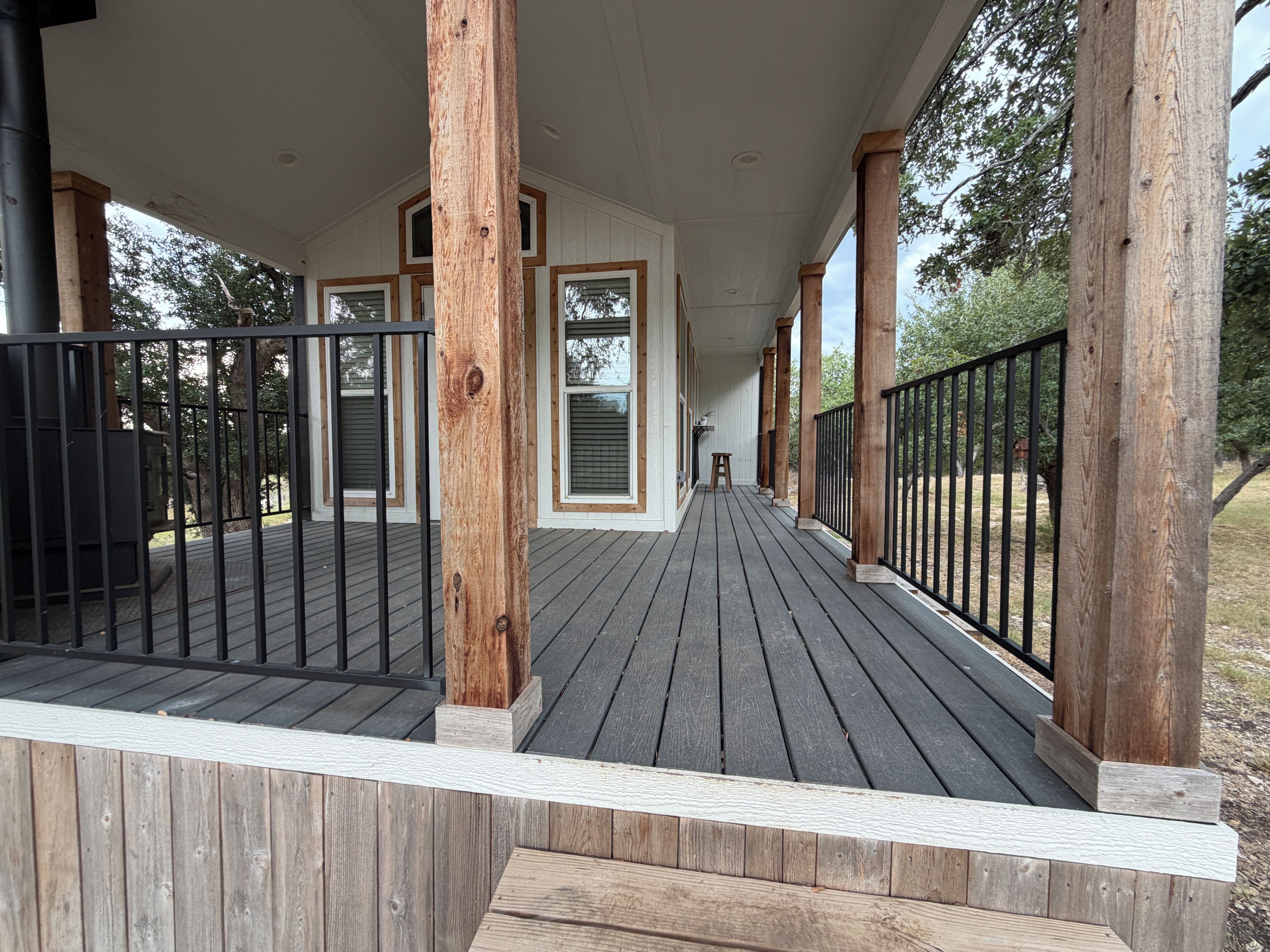 Eine überdachte Holzterrasse mit Geländern, die zu einem Haus mit weißer Fassade und zahlreichen Fenstern führt.