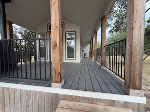 Eine überdachte Holzterrasse mit Geländern, die zu einem Haus mit weißer Fassade und zahlreichen Fenstern führt.