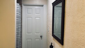 Eine weiße Tür mit rechteckigem Feld, ein Fenster mit schwarzem Rahmen und ein wandmontierter Seifenspender.