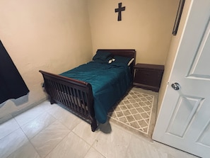 A small bedroom with a single bed, a nightstand, a cross on the wall, and a door. - Cozy 2-bedroom apartment cheaper than a hotel with AC in charming Presidio (Presidio)