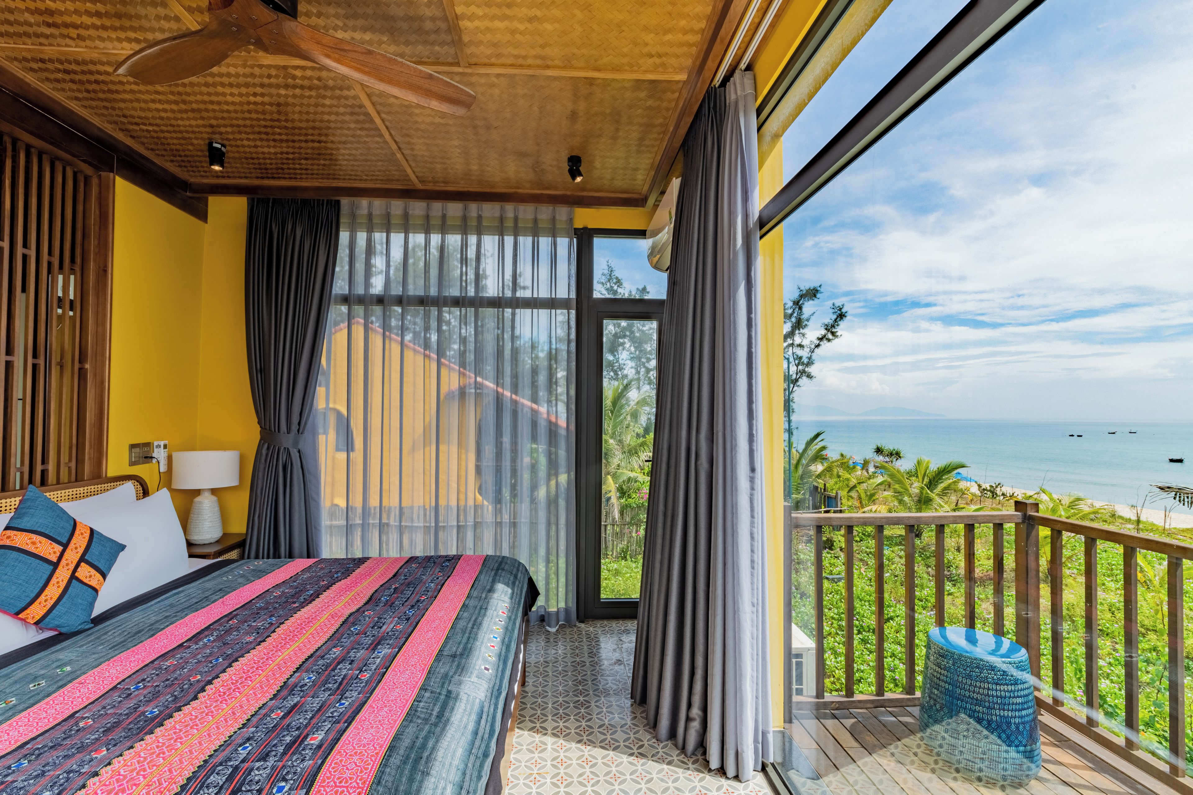 A bedroom with a large bed, a nightstand, a lamp, and a view of the ocean through a sliding glass door.