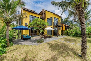 A yellow two-story house with a patio, outdoor furniture, and palm trees. - May Villa 6BR Beachside An Bang Beach Hoi An by Beachside Boutique Homes (Đà Nẵng)