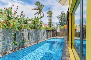 A swimming pool with stone walls and a tiled floor, surrounded by lush greenery and a wooden fence. - May Villa 6BR Beachside An Bang Beach Hoi An by Beachside Boutique Homes (Đà Nẵng)