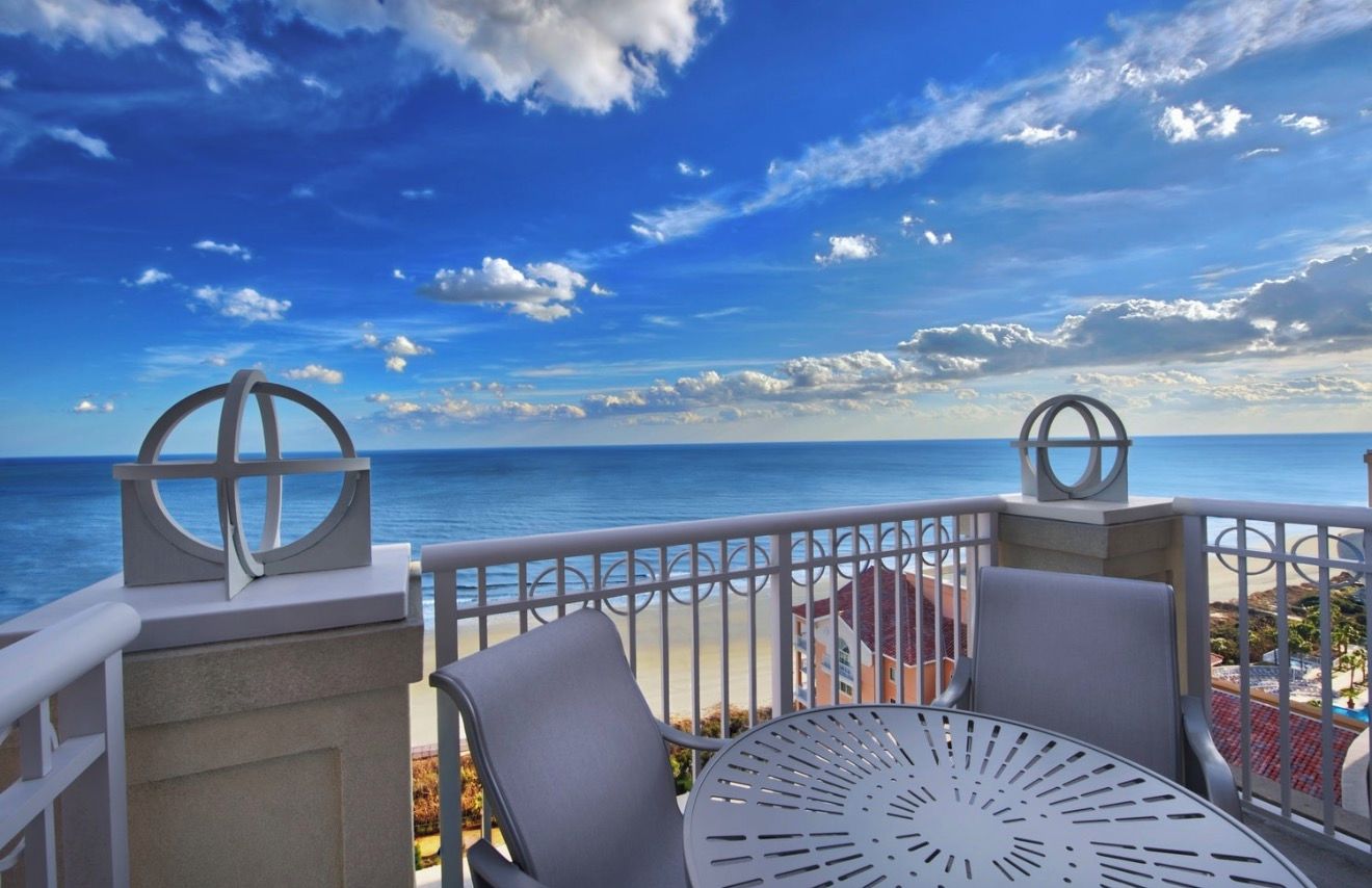 A balcony with a view of the ocean, featuring two chairs and a table.