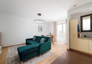 Una sala moderna con un sofá color turquesa, un comedor y una cocina con ventanal.