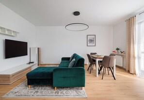 A modern living room with a green sofa, a dining table with chairs, a flat-screen TV mounted on the wall, and a ceiling light fixture. - Olbrachta Cozy Nest Apartment (Warszawa)