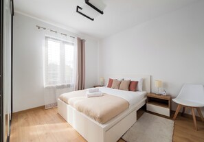 A modern bedroom with a large bed, bedside tables, a chair, and a window with curtains. - Olbrachta Cozy Nest Apartment (Warszawa)