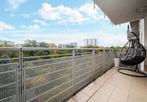 Ein Balkon mit Metallgeländer, einem Hängesessel und Blick auf Gebäude und Bäume.