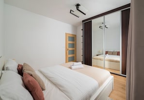 Un dormitorio con cama, una puerta de madera, un espejo y una lámpara en el techo.
