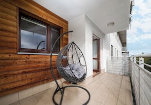 A balcony with a hanging chair, wooden wall, and a view of the sky. - Olbrachta Cozy Nest Apartment (Warszawa)