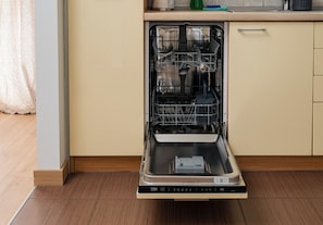 Un lavavajillas abierto en una cocina con suelo de madera y un armario color beige.