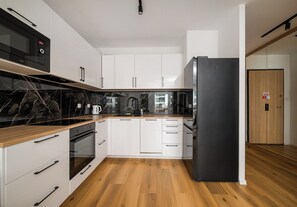 Une cuisine moderne avec des meubles blancs, un réfrigérateur noir et un plan de travail en bois.
