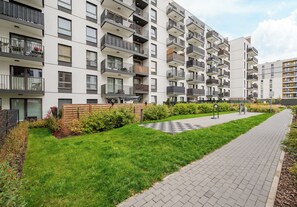 A modern apartment building with multiple balconies, a paved walkway, and a well-maintained garden area. - Ursus Serene Apartment (Warszawa)
