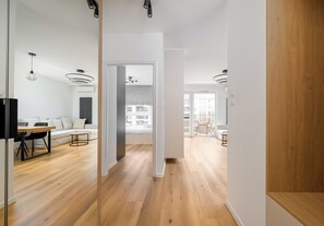 A modern interior with a wooden floor, a dining area with a table and chairs, and a bedroom with a bed and window. - Ursus Serene Apartment (Warszawa)