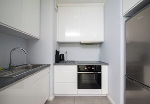 A compact kitchen with white cabinets, a stainless steel sink, a built-in oven, and a refrigerator. - Olszowa 14 Riverside Apartment (Warszawa)