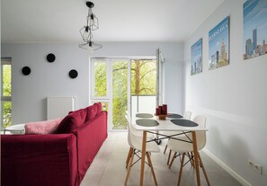 Ein modernes Wohnzimmer mit einem roten Sofa, einem Esstisch mit Stühlen, einer Kristallleuchtre und Stadtansichten an der Wand.