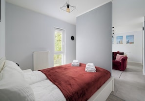 Ein Schlafzimmer mit einem Bett, einem Heizkörper, einem Fenster und Blick ins Freie.