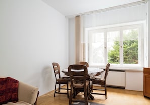 A dining area with a table and chairs, a window with a view of greenery, and a radiator below the window. - Saska Kępa Standard Apartment (Warszawa)