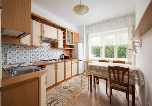 A kitchen with wooden cabinets, a gas stove, and a window with a view of greenery. - Saska Kępa Standard Apartment (Warszawa)