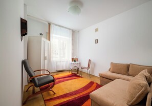 A living room with a sofa, a chair, a table, and a window with curtains. - Saska Kępa Standard Apartment (Warszawa)