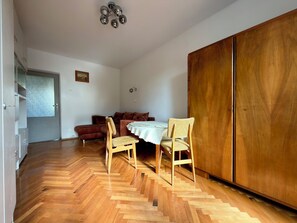 A dining area with a herringbone wooden floor, two wooden chairs, a round table with a white tablecloth, and a brown sofa. - Przestrzenna Comfort Apartment (Wrocław)