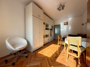 Ein Zimmer mit weißem Stuhl, einem Holztisch, einer Couch und einem Kleiderschrank.