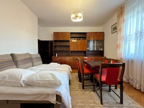 Ein Schlafzimmer mit einem Bett, einem Esstisch mit Stühlen, Holzschränken und einer Hängeleuchte.