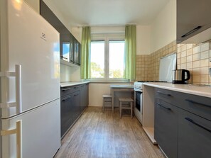 A compact kitchen with a refrigerator, stove, and a small table with a chair. - Przestrzenna Comfort Apartment (Wrocław)