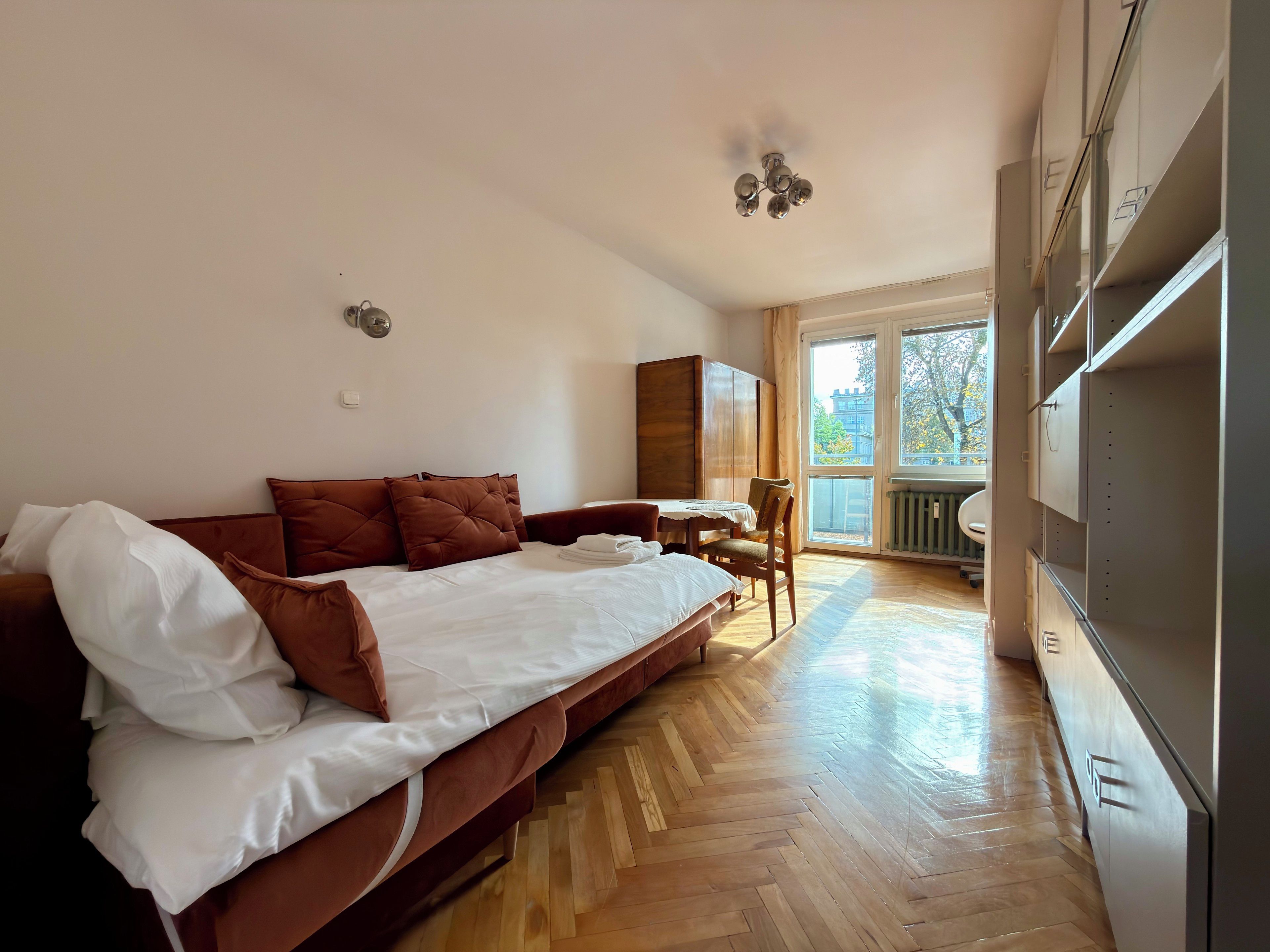 Habitación de hotel con cama, suelo de madera, una mesa de comedor y vistas al exterior.