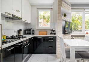 A modern kitchen with a gas stove, microwave, and built-in oven. There is a window providing a view of the outdoors. - Praga Ostrobramska Lavish Apartment (Warszawa)