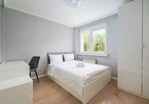 A bedroom with a bed, a chair, a wardrobe, and a window with a view of greenery. - Praga Ostrobramska Lavish Apartment (Warszawa)
