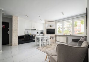 A modern kitchen with white cabinets, a dining area with a white table and chairs, and a living room with a grey sofa. - Praga Ostrobramska Lavish Apartment (Warszawa)