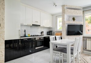 A modern kitchen with white cabinets, a black countertop, and a dining area with white chairs. - Praga Ostrobramska Lavish Apartment (Warszawa)