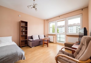 Ein modernes Hotelzimmer mit einer Couch, einem Sessel, einem kleinen Tisch, einem Bücherregal und einem Fernseher.
