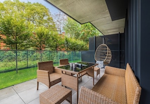 Ein Balkon mit Korbmöbeln, einem Glastisch und einem Hängesessel.