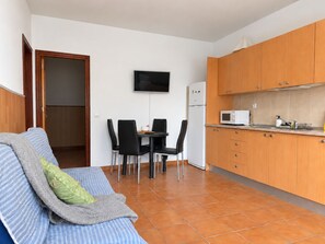 A compact living space with a sofa, a dining table with chairs, a kitchen area with cabinets, a refrigerator, and a flat-screen TV mounted on the wall. - New Listing (Puerto del Rosario)