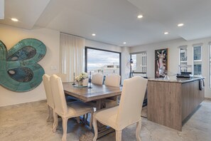 A modern dining area with a wooden table, white chairs, and a large abstract wall art piece. - Modern Ocean View 2BR Condo Resort-Style Pool, Gym & Prime Cabo Location (Cabo San Lucas)