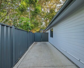 A narrow concrete pathway leading to a building with a grey metal fence on one side and a white exterior wall on the other. - Modern 2BR Hideaway Near Coffs Harbour CBD (Coffs Harbour)