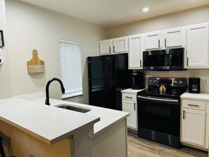 A modern kitchen with white cabinetry, a black refrigerator, a microwave, a stove, and a coffee maker. - Spacious 4-bedroom townhome with AC in peaceful Kissimmee FL Gated Community, (Kissimmee)