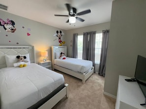 Ein Hotelzimmer mit zwei Betten, einem Deckenventilator, einem Fernseher und Mickey Mouse Dekoration.