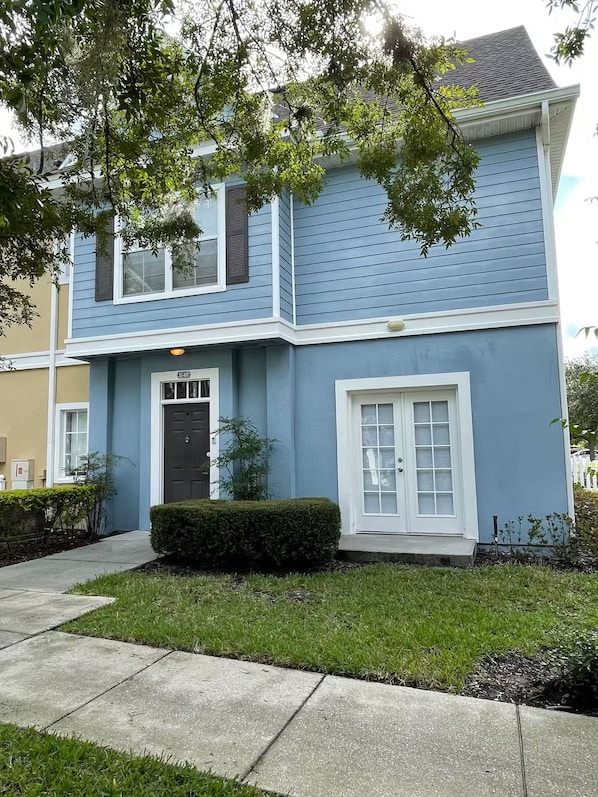 A two-story house with a blue exterior, a front door, and a small front yard with a hedge. - Spacious 4-bedroom townhome with AC in peaceful Kissimmee FL Gated Community, (Kissimmee)
