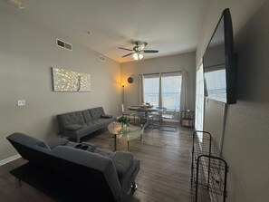 A modern living room with a grey sofa, a glass coffee table, and a dining area with a round table and chairs. - Spacious 4-bedroom townhome with AC in peaceful Kissimmee FL Gated Community, (Kissimmee)